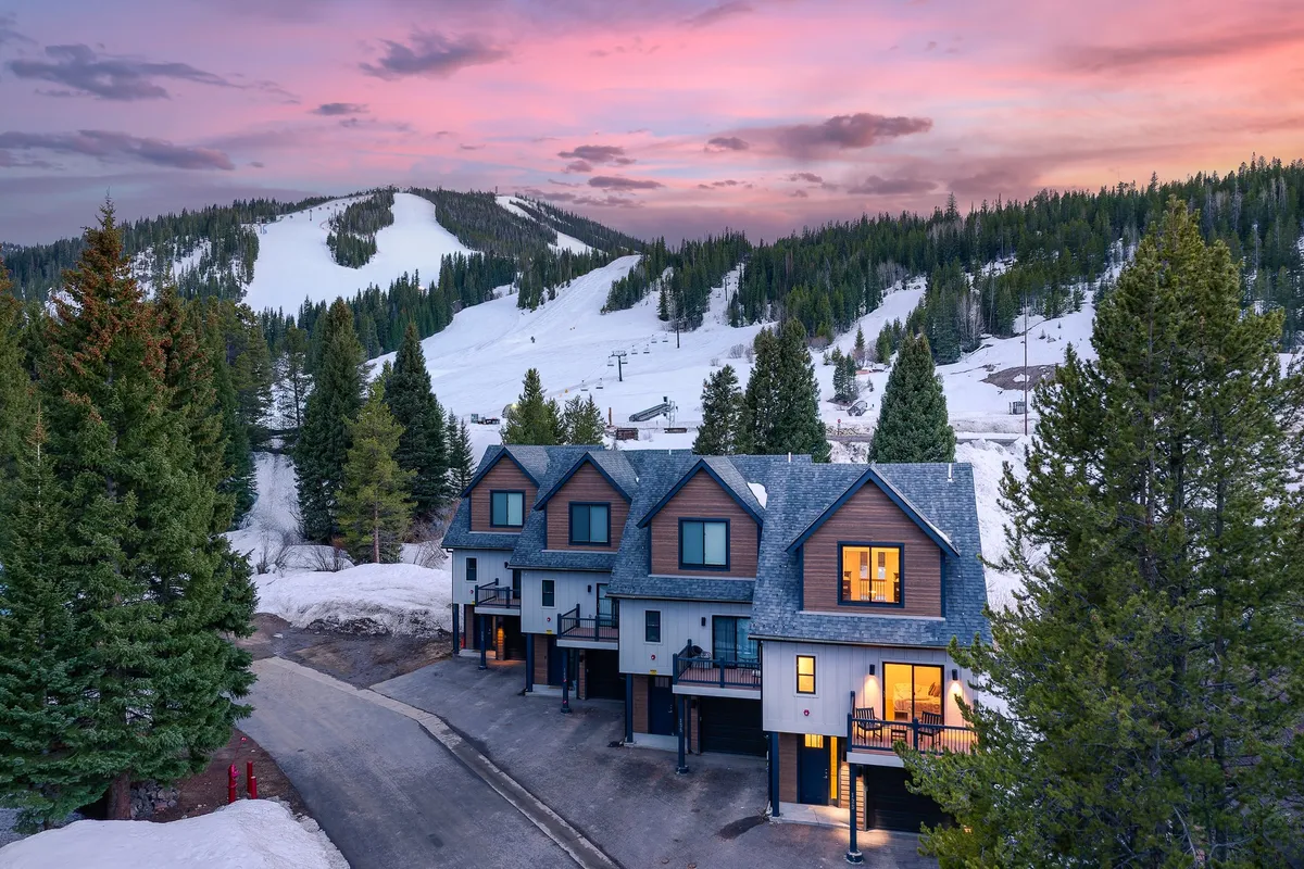 The image showcases a luxury villa set against the backdrop of snowy mountain slopes, with the sun setting in a breathtaking sky. The villa's balcony provides a perfect spot to take in the view, while the scene evokes both the excitement of daytime skiing and the promise of warm, cozy evenings inside.