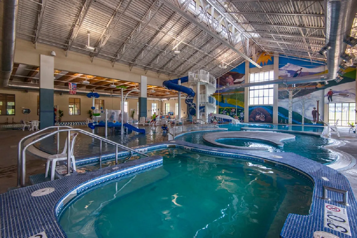A vibrant indoor pool scene where children gleefully slide down waterslides, splash in the pool, and families relax together, surrounded by colorful murals—perfect for a rainy day or post-adventure fun.