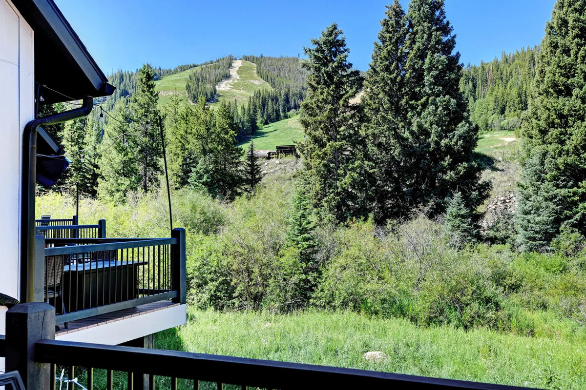 This image captures a serene view of the mountain landscape from a balcony, surrounded by dense trees. The setting invites guests to relax on the balcony while taking in sunsets or early morning mountain vistas, evoking both adventure and tranquility.