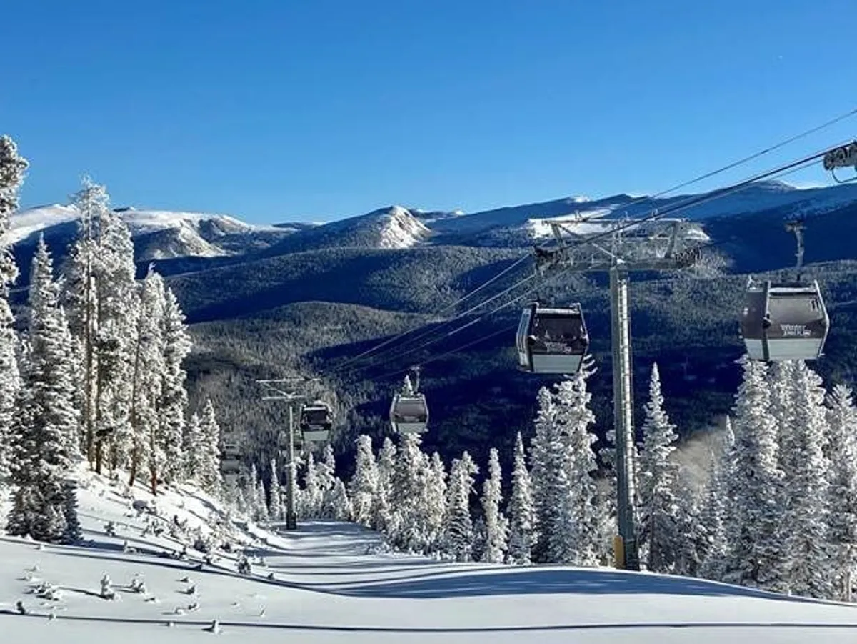 This image features ski lift gondolas moving over snow-covered trees with a dramatic mountain range in the background. The snowy landscape and visible ski infrastructure immediately evoke the excitement of slopeside adventure and the proximity to Winter Park Resort.