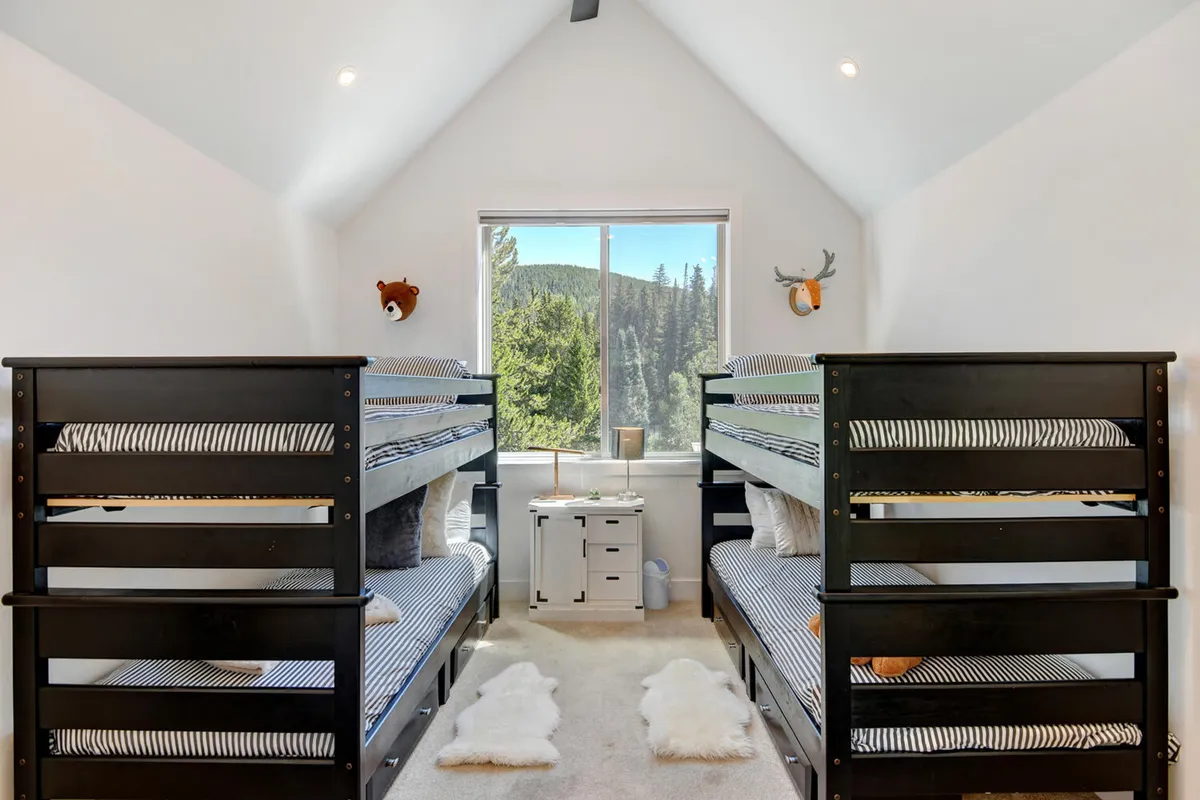 A playful bedroom with twin bunk beds, a large window offering a mountain view, decorative animal heads, and a nightstand. The room is cozy and fun, ideal for families or groups of friends.
