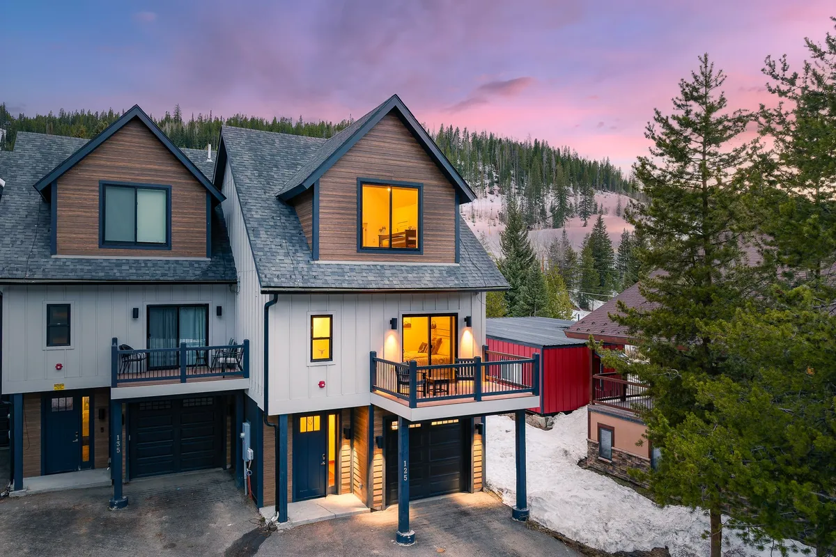 This exterior image features a spacious balcony with comfortable seating, large windows that invite natural light in, and a stunning backdrop of mountains and surrounding trees. The space is perfect for gatherings, sunset views, and outdoor barbecues, echoing the après-ski or summer evening atmosphere.