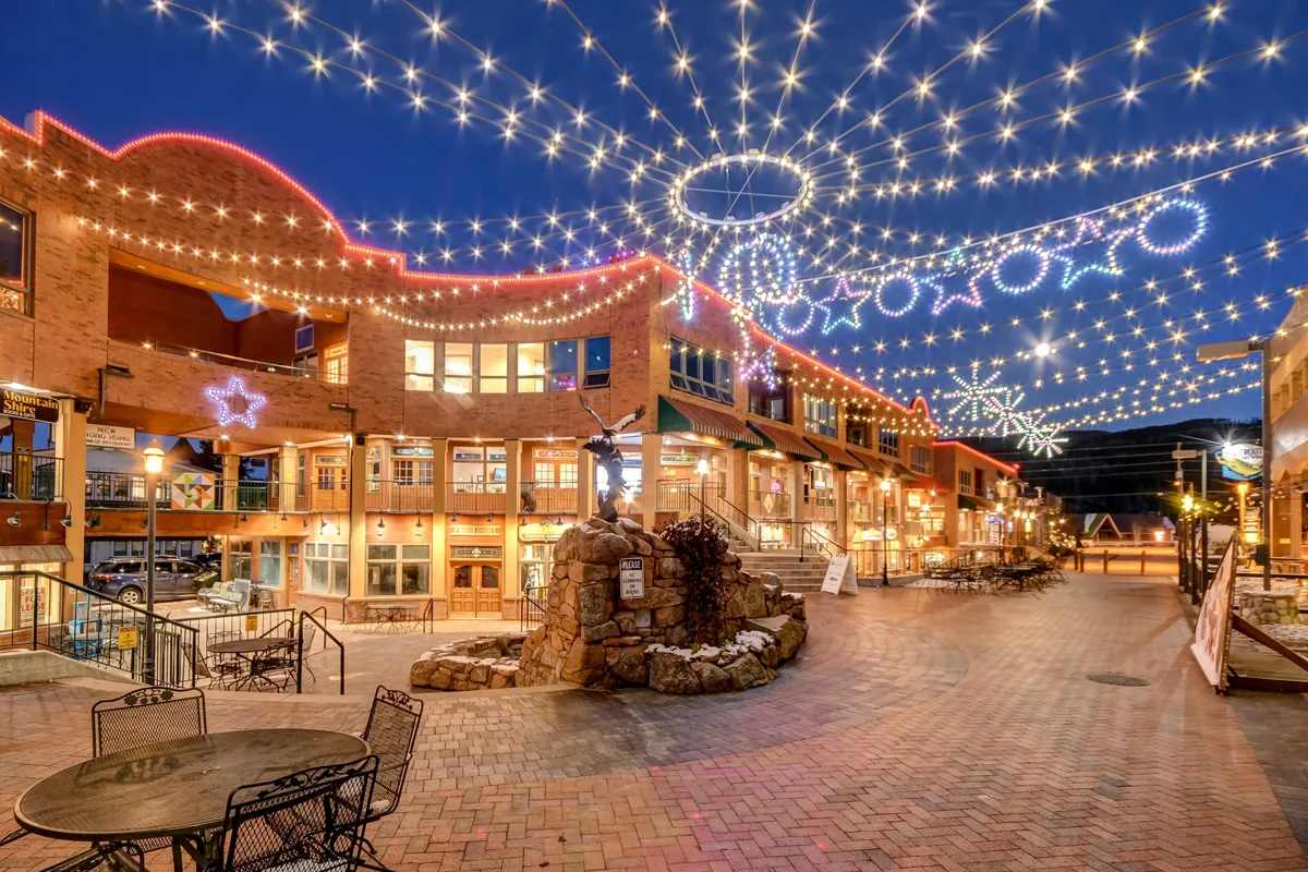 An exterior shot of the resort base area alive with twinkling string lights, festive architecture, and people strolling, shopping, and socializing—reflecting the joyful, communal energy of local events and activities.