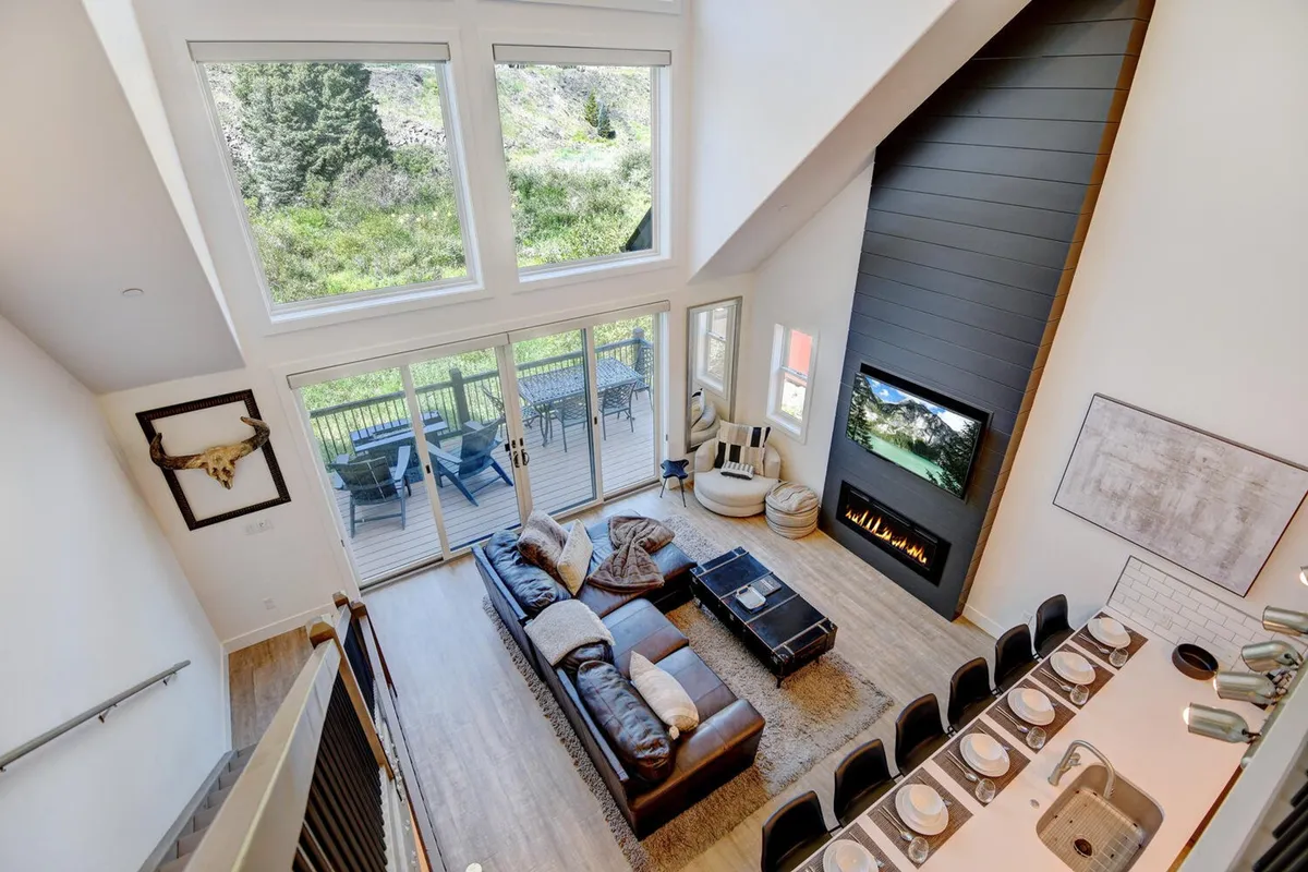 An open-concept dining area with a large wooden table, comfortable seating, and expansive windows letting in natural light. The dining table is set in a warm, welcoming atmosphere, ideal for shared meals and gatherings. A fireplace adds to the cozy ambiance.
