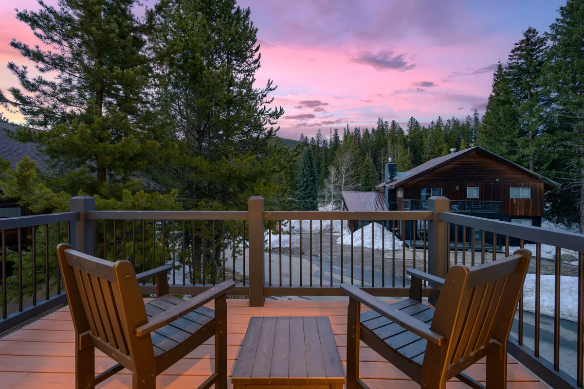 A peaceful outdoor setting with wooden chairs and a table nestled among trees, offering sunset views and a clear connection to the natural environment. The distant cabin and surrounding greenery highlight the property’s immersion in nature.