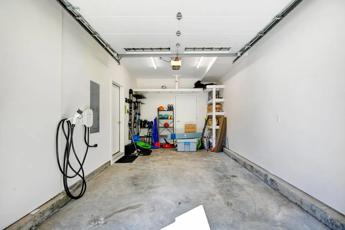An interior shot of a pristine garage featuring an electric vehicle charger, neatly arranged storage shelves, and a clean concrete floor. The space is bright and organized, highlighting areas for secure gear storage and easy parking.