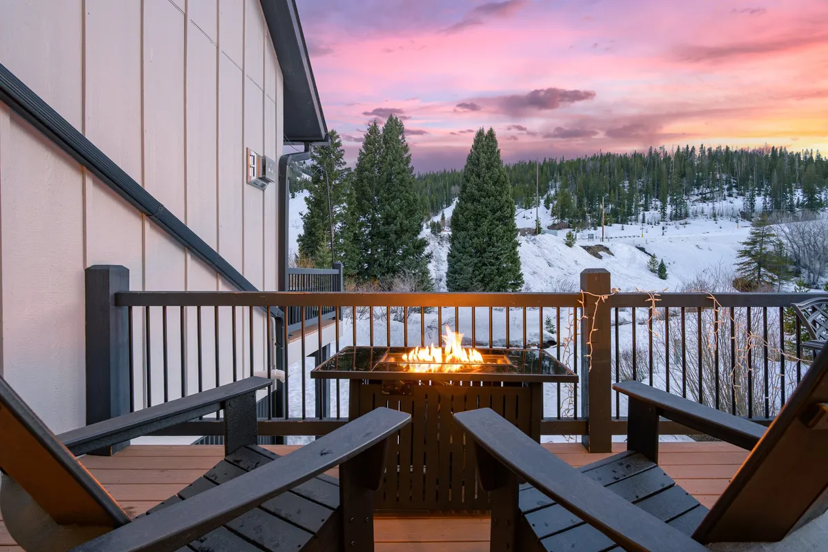 An exterior scene with a fire pit, adirondack chairs arranged in a circle, and sweeping views of the mountain landscape. The mood is relaxed and serene, ideal for enjoying sunsets, warming up after a day outdoors, and intimate group conversations.
